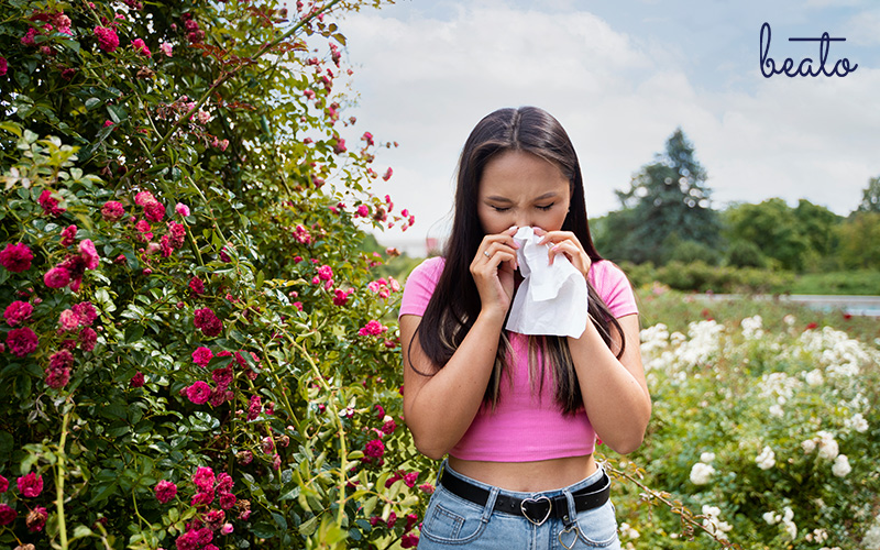 woman beside flowers sneezing on a tissue